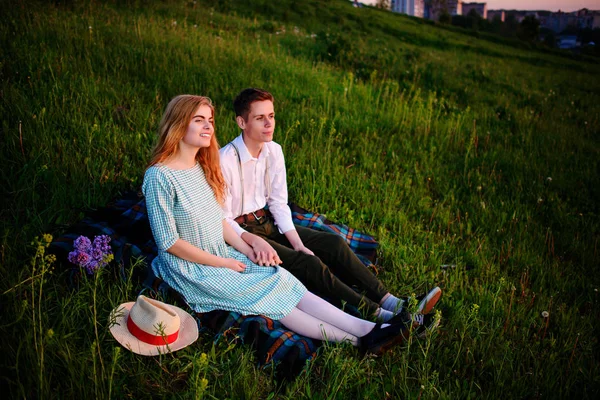 Νέοι ζευγάρι κάθεται στο plaid στο πάρκο και να εξετάσουμε το ηλιοβασίλεμα — Φωτογραφία Αρχείου