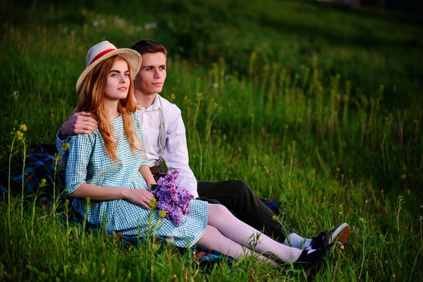 Young couple sitting on the plaid in the park and look at the sunset — Stock Photo, Image