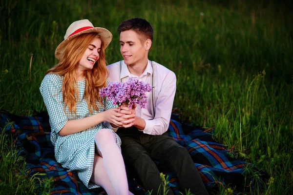 Genç çift, park ve günbatımı bakmak ekose oturan adam kız arkadaşı leylak bir buket verir — Stok fotoğraf