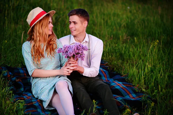 Genç çift, park ve günbatımı bakmak ekose oturan adam kız arkadaşı leylak bir buket verir — Stok fotoğraf