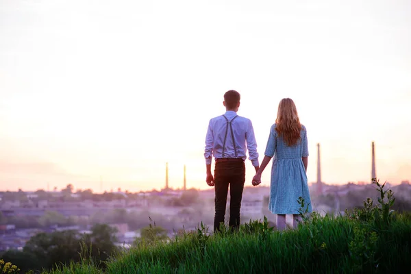 Young couple is holding hands on a background sunset — Stock Photo, Image