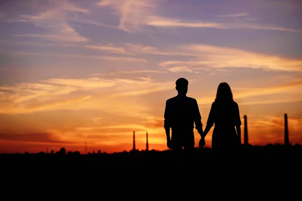 若いカップルが手を繋いでいる日没のシルエットをバックに — ストック写真