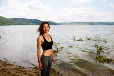 Güzel bir sportif kadın spor giyim bir göl kıyısında duran ve bir egzersiz için hazırlanıyor