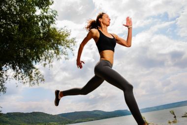 A beautiful sporty woman runing on the shore of a lake in sportswear. Girl is exercising clipart