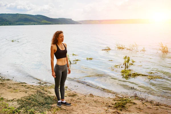 Krásná sportovní žena stojící na břehu jezera v sportswear a příprava cvičení — Stock fotografie