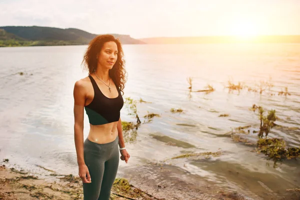 Güzel bir sportif kadın spor giyim bir göl kıyısında duran ve bir egzersiz için hazırlanıyor