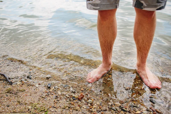 Cerca de fondo de los pies del hombre de pie en un agua clara con fondo de guijarros —  Fotos de Stock