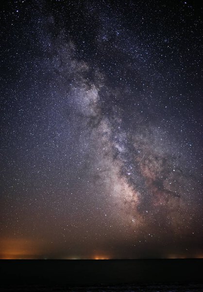 Фон яркого ночного звездного неба с Млечным Путем на нем и светом над водой
