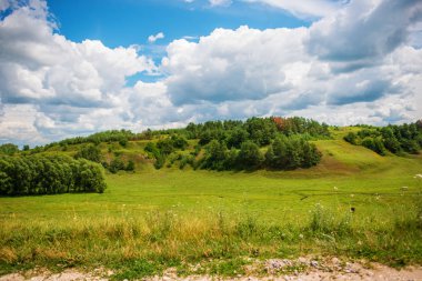 Küçük tepelerdeki yeşil çayır ve bulutlu mavi gökyüzü