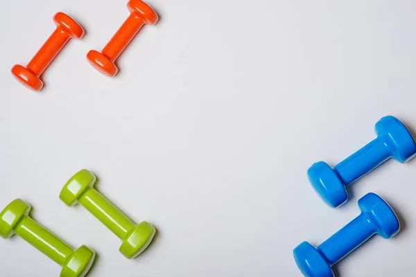 Muitos azul verde e uma laranja nos halteres do meio em um fundo branco, conceito se preparando para fitness equipamentos esportivos vista superior mock up — Fotografia de Stock