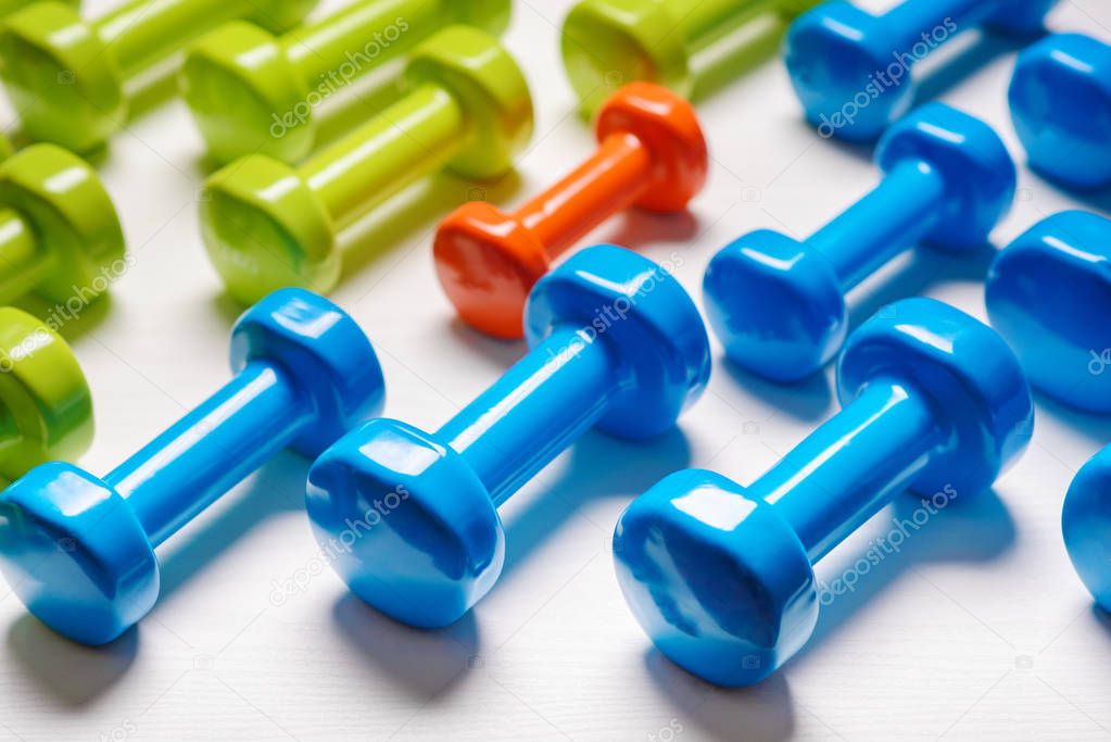 many blue green and one orange in the middle dumbbells on a white background ,concept preparing to fitness sports equipment top view mock up