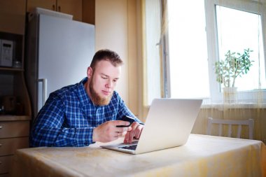 Ofiste cama tabloda, dizüstü bilgisayar ve akıllı telefon kullanan adam.