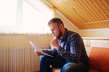 Genç yakışıklı adam kanepede oturan ve bir çalışma kağıdı saatler.