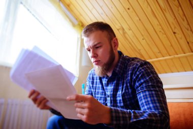 Genç yakışıklı adam kanepede oturan ve bir çalışma kağıdı saatler.