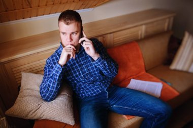 Genç ciddi adam evde kanepede rahat oturan onun telefonda konuşuyor.