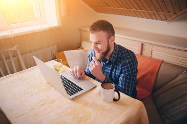 Onun laptop içinde internette sörf rahat genç profesyonel bir yemek odası.