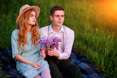 Genç çift, park ve günbatımı bakmak ekose oturan adam kız arkadaşı leylak bir buket verir.