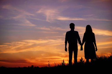 young couple is holding hands on a background sunset silhouette. clipart