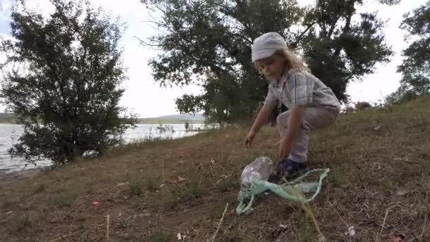 The little boy collects debris on the lake slow motion — Stock video