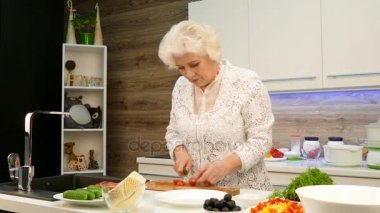 Gri saçlı Olgun kadın mutfakta bir salata için kiraz domates kesmek.