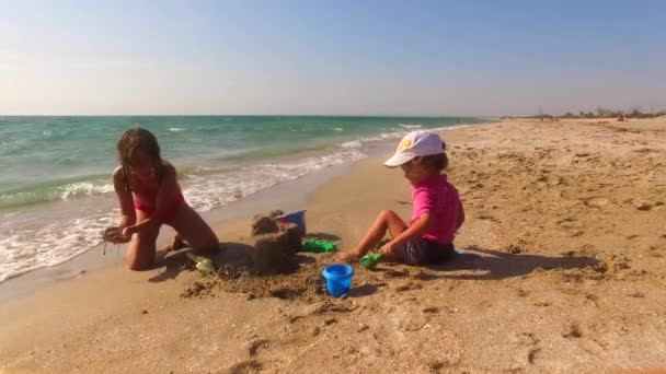 Due bambini che costruiscono il castello di sabbia sulla spiaggia — Video Stock