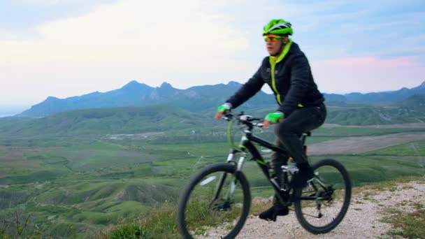 Hombre - un turista conduce a la cima de la montaña en una bicicleta deportiva. Hay una vista del valle de la montaña y el mar en el horizonte . — Vídeo de stock