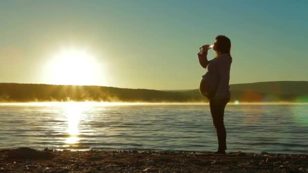 Embarazada en la playa bebiendo agua de una botella . — Vídeo de stock