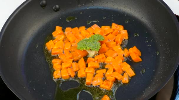 Bak stukken van wortelen in de olie in een koekenpan met broccoli — Stockvideo