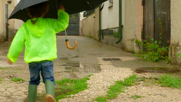 Boy with an umbrella running around the yard in rubber boots — Stock Video