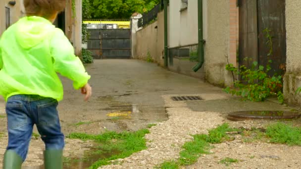 De jongen in de regenjas loopt rond de werf in rubberen laarzen — Stockvideo