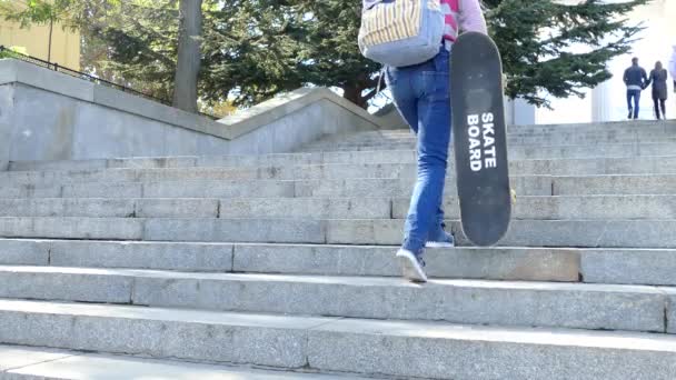 Uma menina sobe os degraus e segura um skate em sua mão — Vídeo de Stock