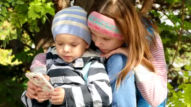 Uma menina com um menino está usando um smartphone . — Vídeo de Stock