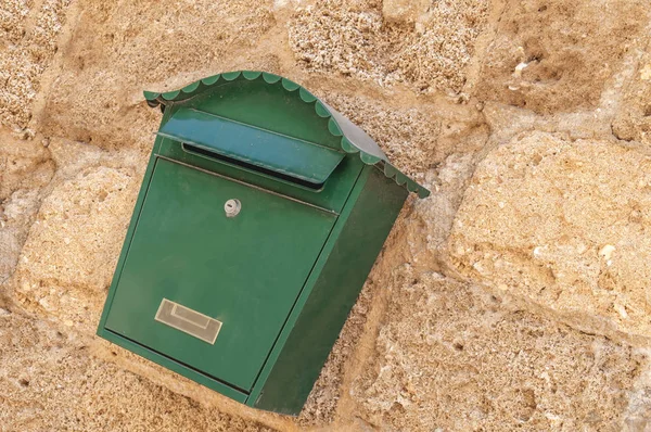 Green metal mail box hanging on left side of yellow concrete house wall