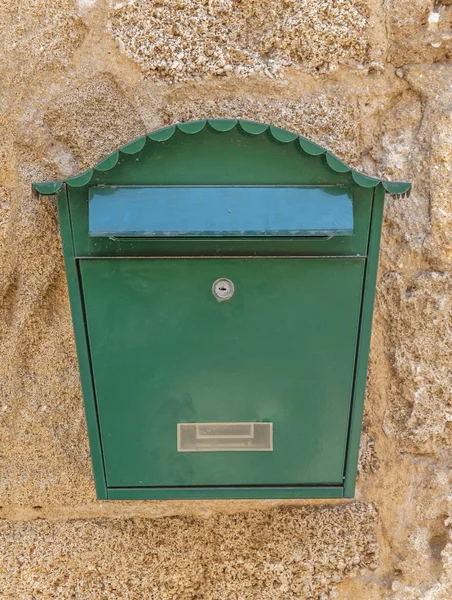 Green metal mail box hanging on yellow concrete house wall