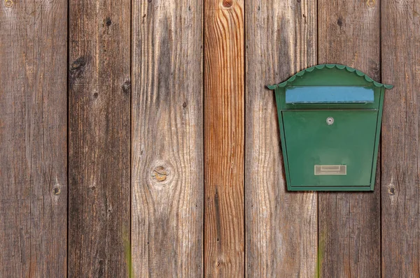 Green metal mail box hanging on right side of wooden house wall