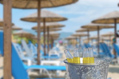 Kova çok şezlong ve şemsiye ile büyük halk plajı, dört bira şişesi bardak içecek