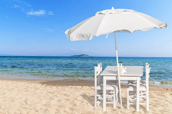 Деревянный стол с четырьмя стульями на прекрасном песчаном пляже и голубом небе — стоковое фото