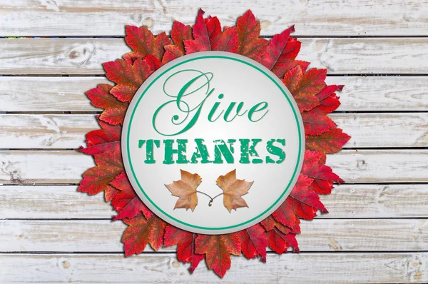 Give thanks written in circle inside red leaves white wooden background