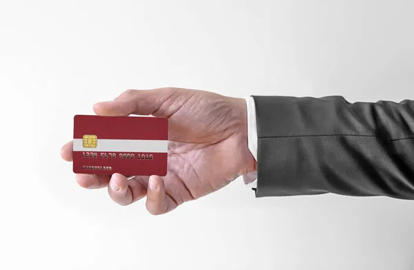Bankovní kreditní plastová karta s vlajkou Lotyšska držící muže v elegantním obleku — Stock fotografie