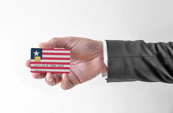 Banco tarjeta de crédito de plástico con bandera de Liberia la celebración del hombre en traje elegante — Foto de Stock