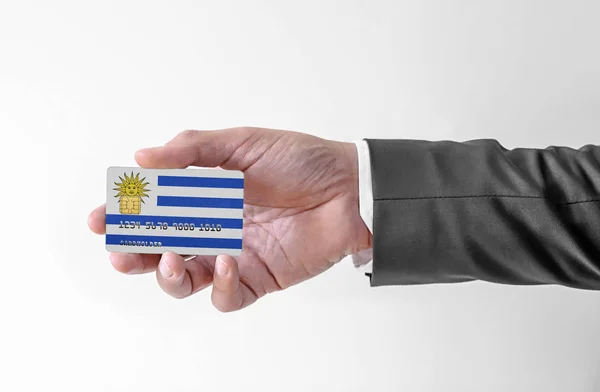 Banco cartão de crédito plástico com bandeira de Uruguai segurando homem em terno elegante — Fotografia de Stock