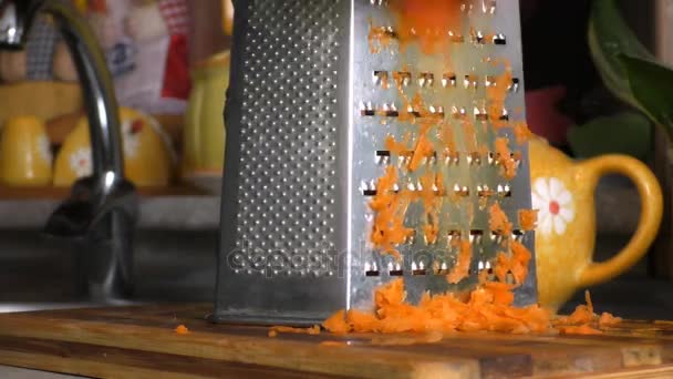 A fêmea esfrega cenouras em um ralador em uma tábua de corte — Vídeo de Stock
