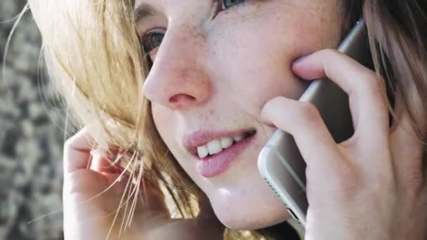 La chica sonriente europea hablando por teléfono. Conversación positiva de una chica en el teléfono. Comunicación moderna y redes sociales — Vídeos de Stock