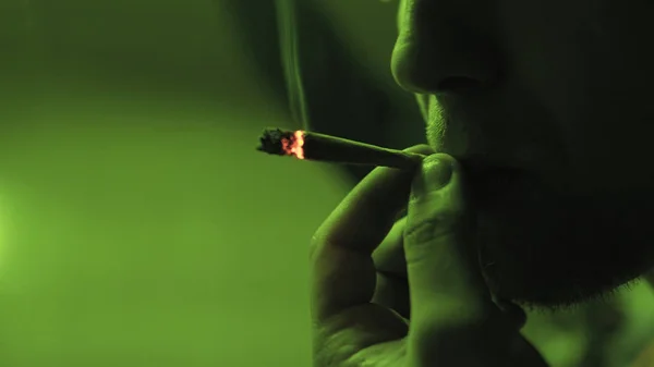 Genç bir adam haddelenmiş jointer yeşil ışık yakın çekim içinde içinde esrar tomurcukları Sigara. — Stok fotoğraf