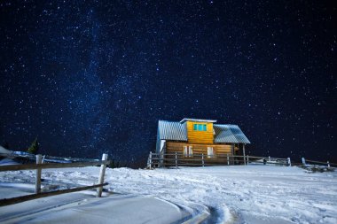Güzel bir gece kış yıldızlı gökyüzü ahşap ev, uzun pozlama fotoğraf kırsal kabinde küçük köy yakınındaki karlı yarda ve gece yarısı yıldız toplayan