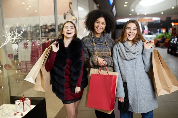 Heureuses jeunes femmes multiethniques élégantes avec des sacs à provisions marchant dans un centre commercial avec des sacs écologiques en papier. Concept de consumérisme des filles caucasiennes et afro-américaines. Sacs avec espace de copie pour le placement de la marque . — Photo