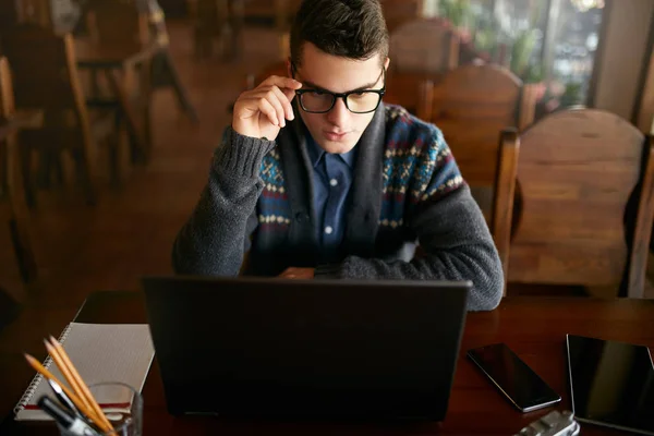 Businessman working with documents on laptop tablet and smart phone on table. Freelancer browsing web in cafe. Handsome hipster in knitted sweater holding glasses in his hand. Poor eyesight threatment