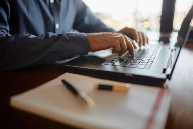 Yakın çekim fotoğraf tipik dizüstü klavye ve touchpad kullanarak beyaz erkek el. Defter ve kalem çalışma alanının ön plan üzerinde. Bilgisayarda çalışan iş adam. Hiçbir yüz görünümü izole.