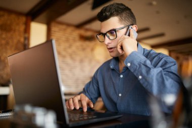 Laptop ile çalışma ve Office istemci ile telefonda konuşurken genç serbest meslek. Gözlük yakışıklı beyaz işadamı müzakereler yolu ile telefon görüşmesi yapar. Çoklu görev iş kavramı.