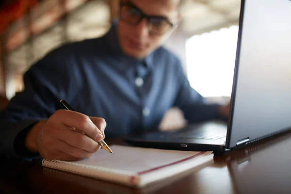 Primo piano di uomo scrittura a mano su taccuino di carta. Giovane uomo d'affari in bicchieri prendere appunti in blocco note con stilografica premium costoso elegante. Un contratto firmato da un uomo. Studente che lavora su laptop . — Foto Stock